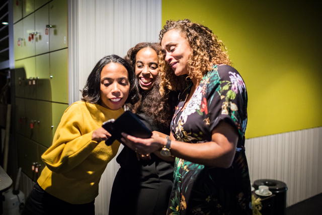 Drie vrouwen bekijken samen een telefoon en lachen vrolijk